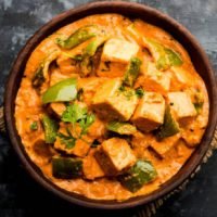 Malai or achari Paneer in a gravy made using red gravy and green capsicum. served in a bowl. selective focus